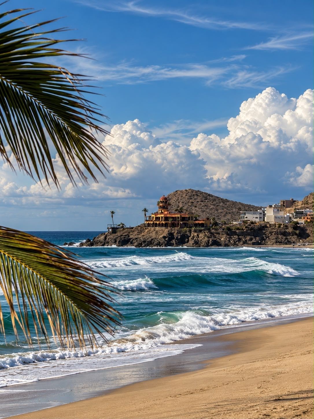 Playa Los Cerritos on a clear afternoon, the rocky point and its hillside houses beyond the breaking surf